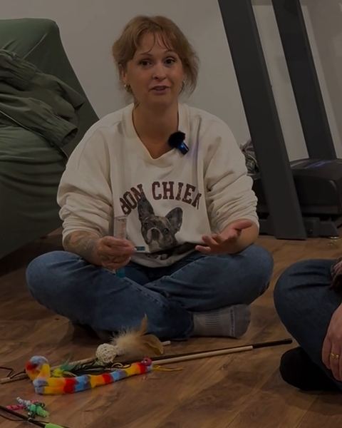 Stéphanie Portelance sits cross-legged on a wood floor in a white sweatshirt and speaks to the camera.